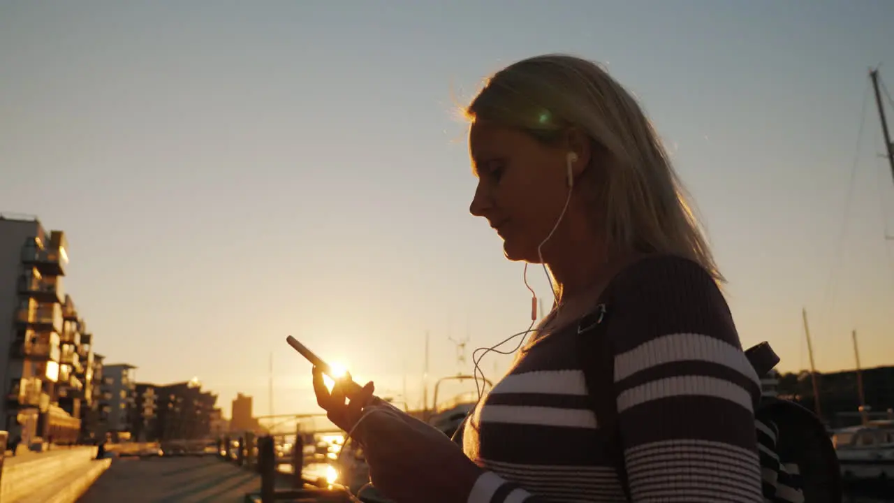 A Woman In Headphones Uses A Smartphone On The Pier On The Background Of Private Yachts At Sunset Th