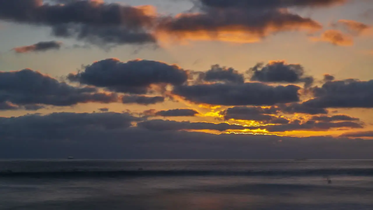 Amazing beautiful golden sunset timelapse with light rays beaming through thick clouds over calm ocean waves flowing