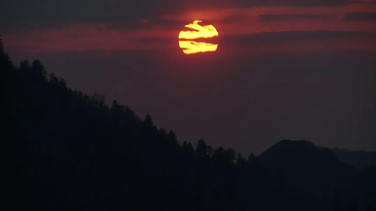 The sun slowly sets through the clouds behind a silhouetted ridge