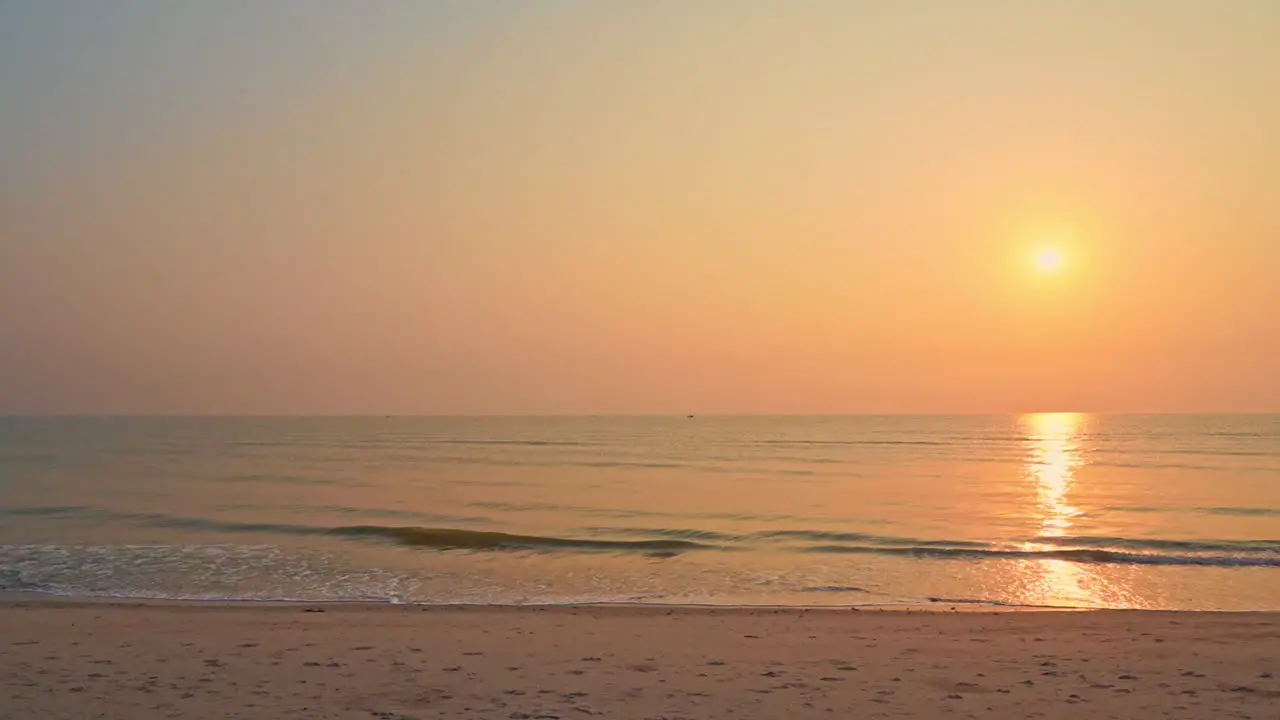 Slowmo Golden sun reflects on turquoise ocean surface as waves hits pink sandy beach