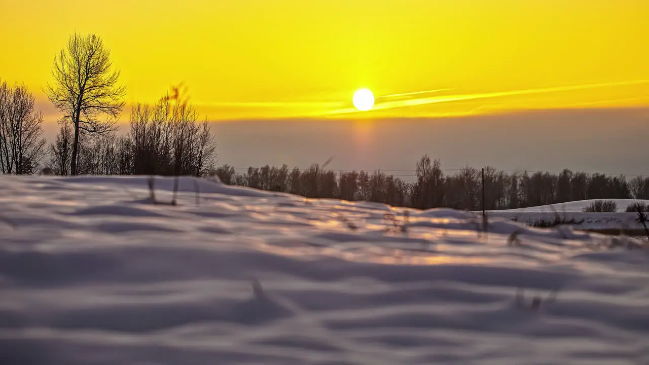 Ground level time-lapse of setting sun into yellow sky over snowy landscape