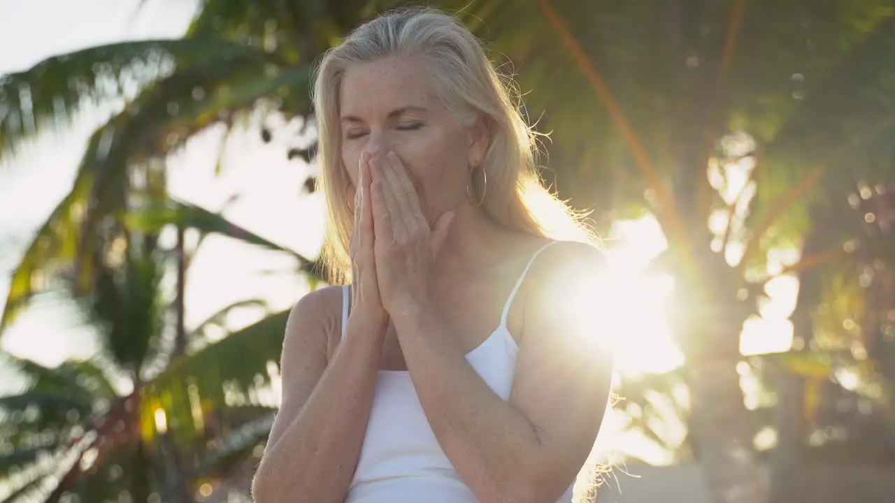 Sun shines into the camera lens as blonde mature woman looks amazed off camera then smiles at camera and then looks off camera again with palm tree behind