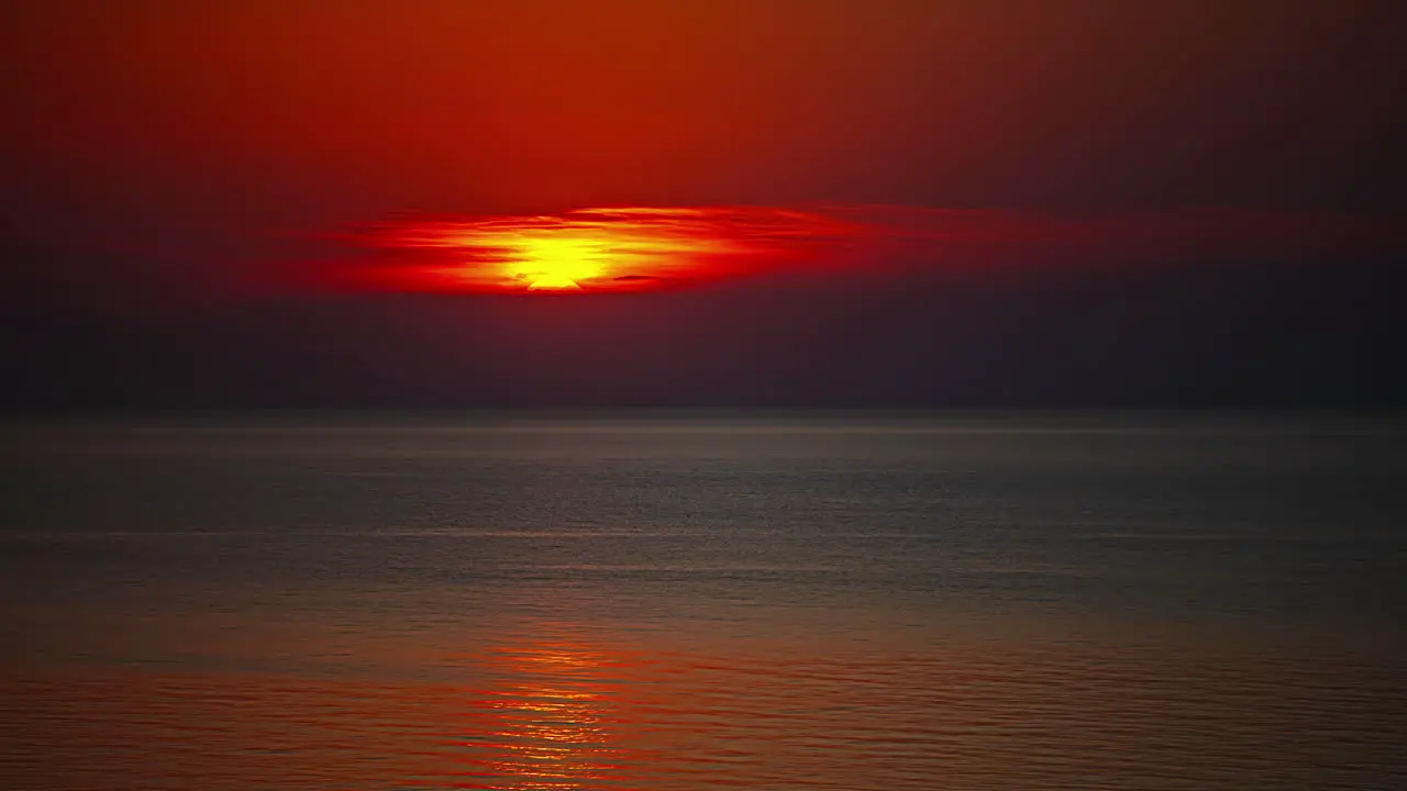 Beautiful red sun setting in the horizon beyond calm waves Hyperlapse