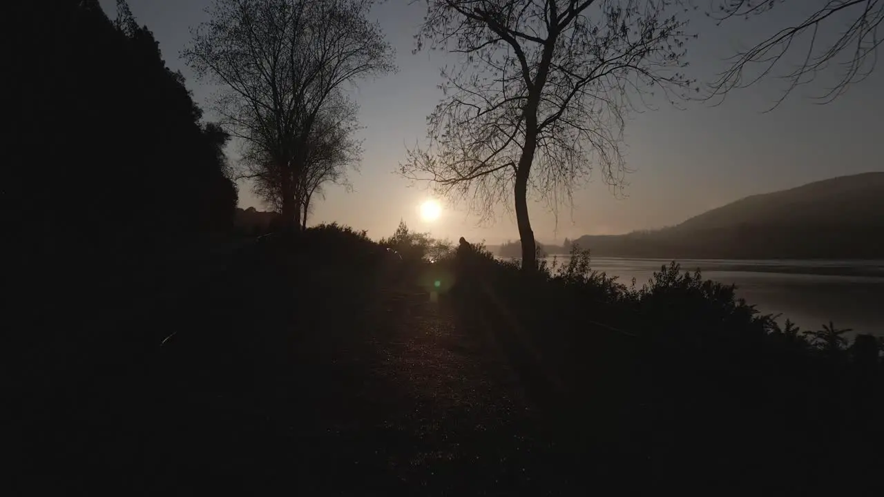 Drone shot of sunrise by the lake side of the highway with a silhouette of a visitor and his motorbike