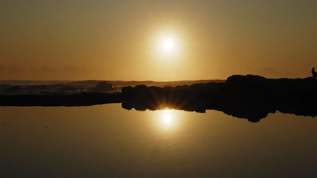 Slow motion shot of golden sunrise over ocean reflected in mirror-like rock pool