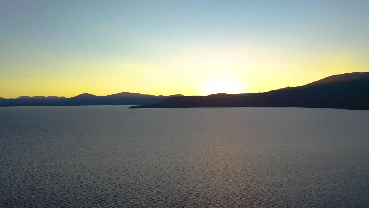 Sun Rising Over Lake with Mountains Silhouette in Background