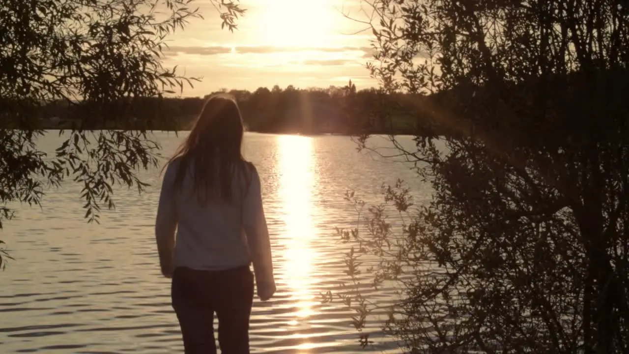 Woman silhouette walking towards rippling lake at sunset