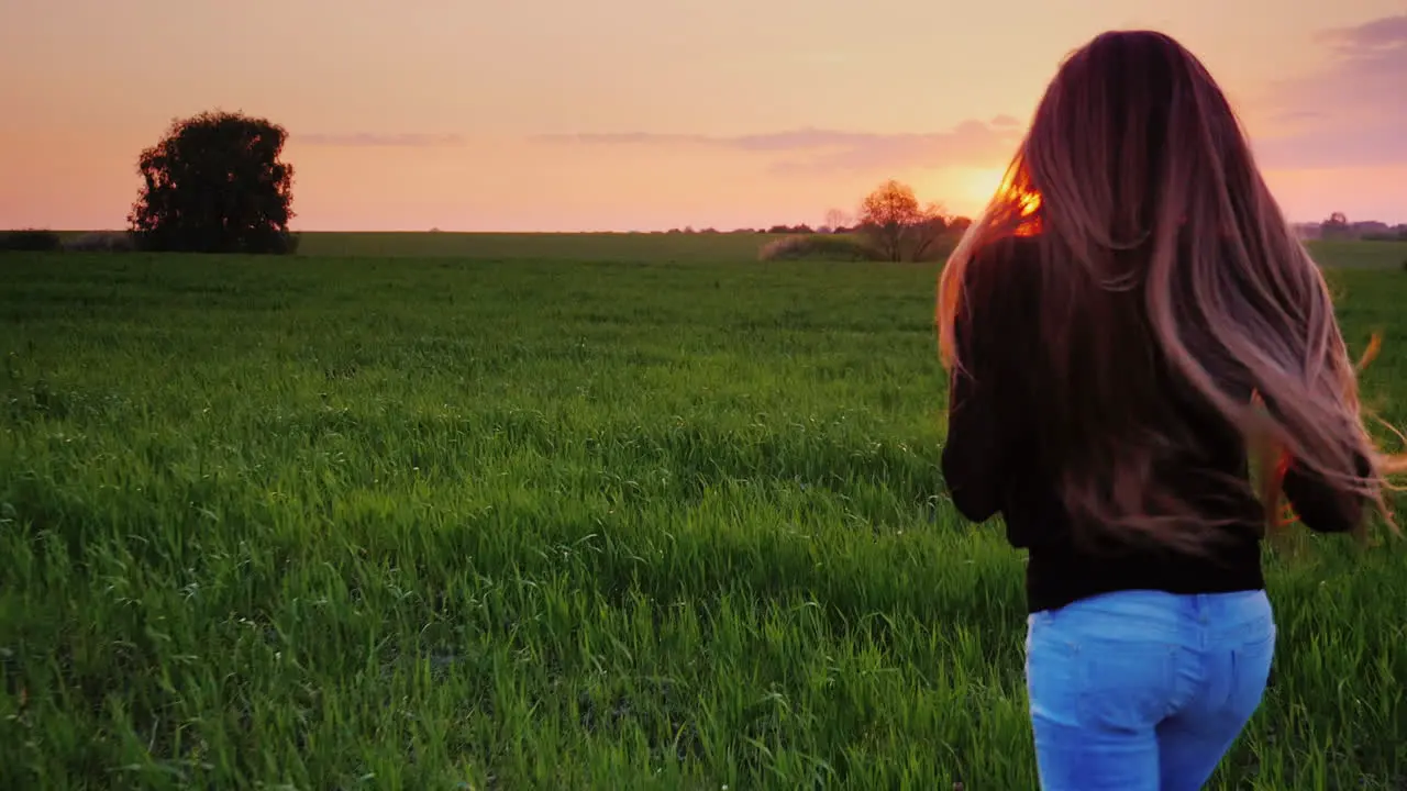 A Young Woman With Beautiful Long Hair Runs Along The Green Field