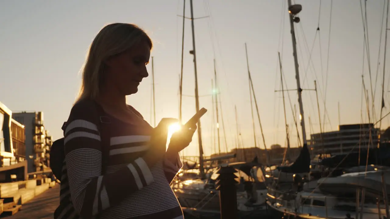 Silhouette Of A Woman Using A Smartphone Near The Pier Where Many Yachts Are Moored