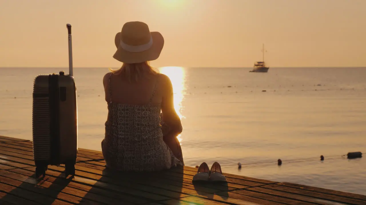 A Woman Looks At The Ship In The Distance Sitting On The Pier Near Her Luggage The Travel Concept