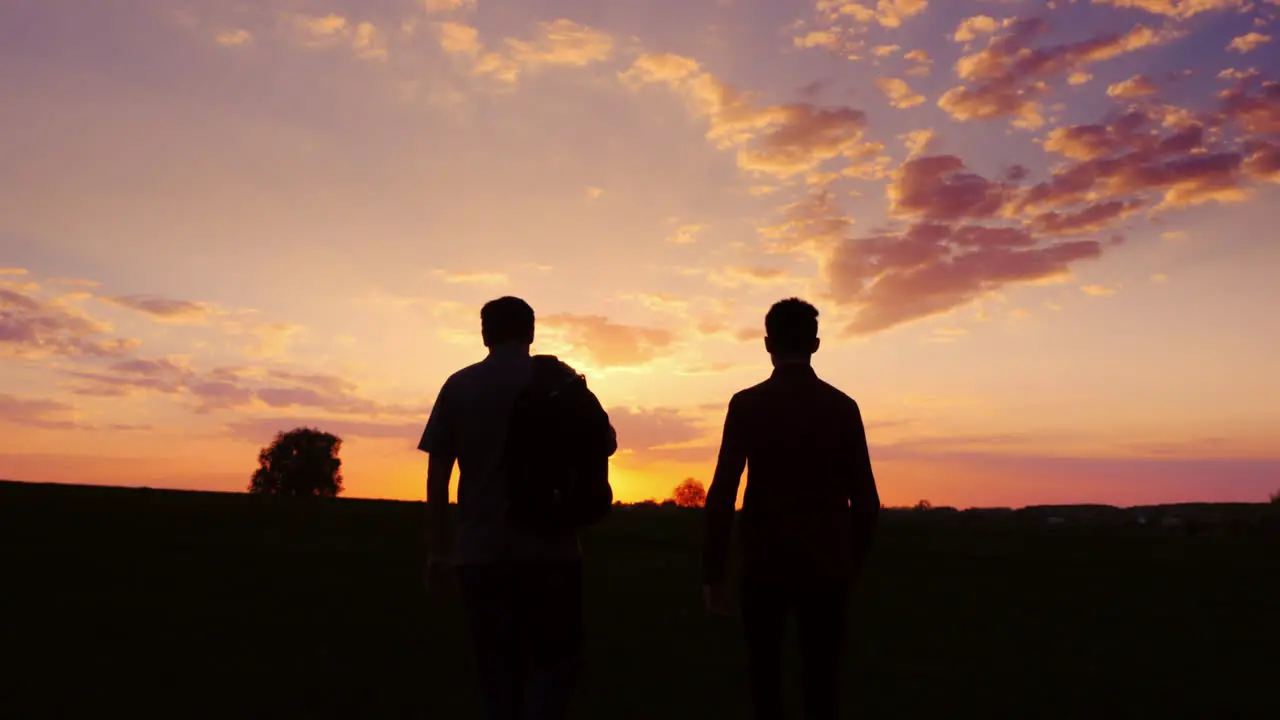 Father And Son Are Walking Along The Field At Sunset