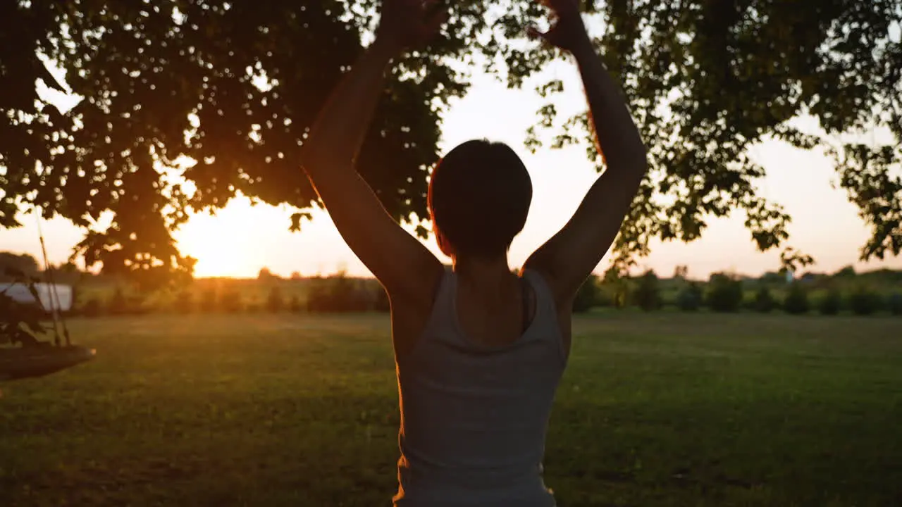 Short-haired woman does jumping jacks while facing a beautiful sunset