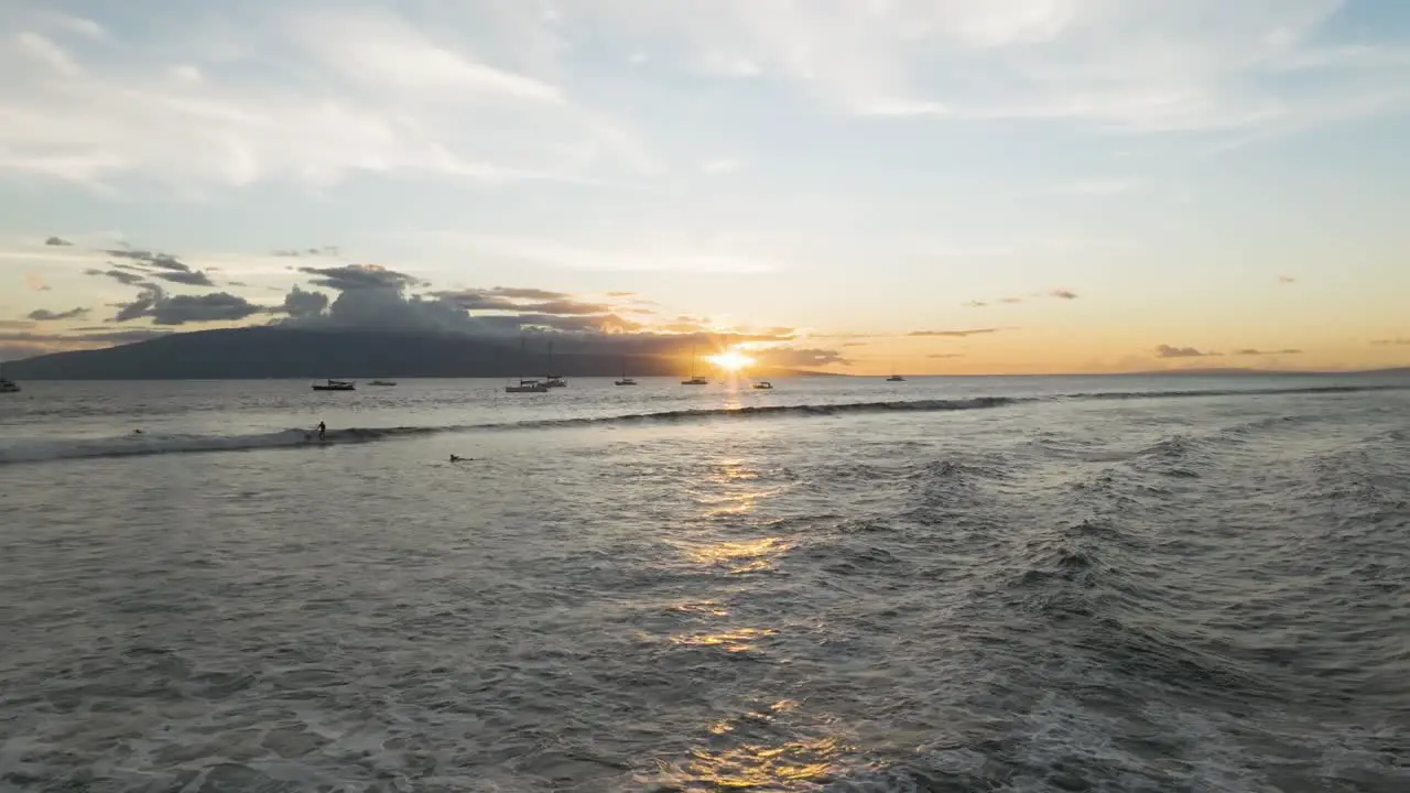 Sun sets behind Lanai Island and anchored boats as surfer whips on Lahaina waves