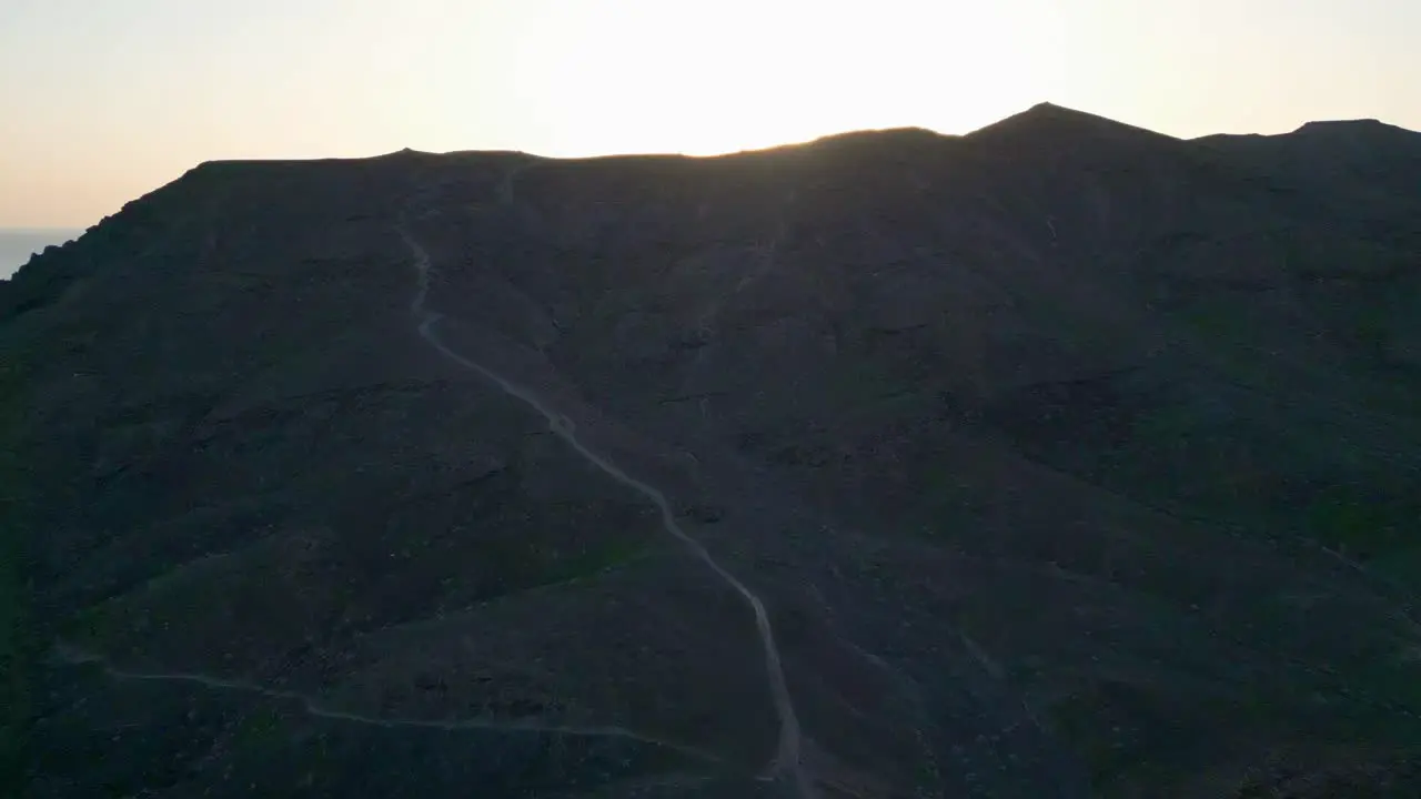 Aerial shot following foot trail to the top of a mountain revealing the beautiful sunset