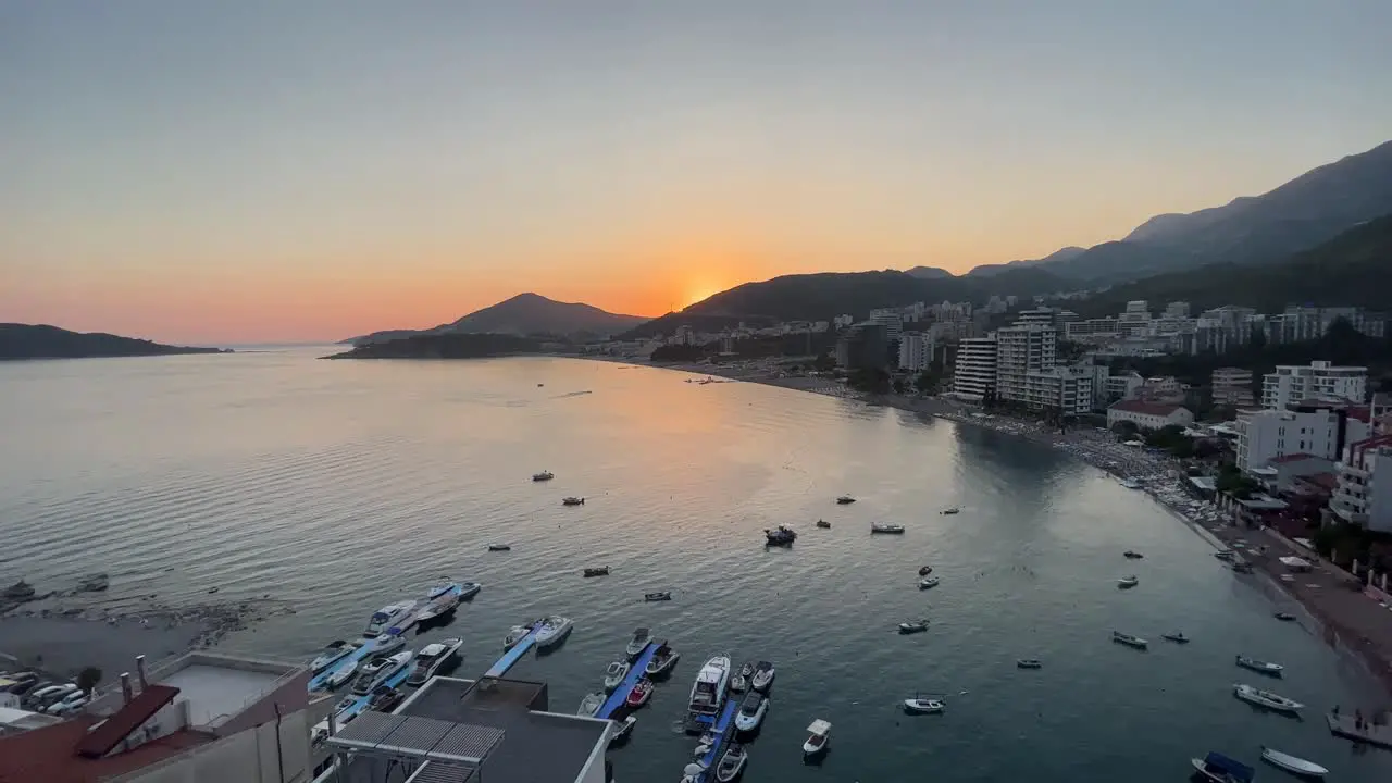 Lovely sunset over rafailovici in montenegro high flying drone shot in the evening on a sunny day during sunset sun setting over the mountain with boats and cars in the view