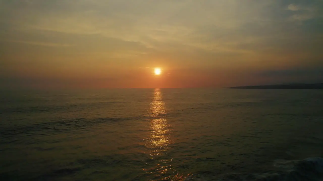 Aerial seascape view of waves crashing on a tropical coastline wiht palm trees silhouettes at sunset