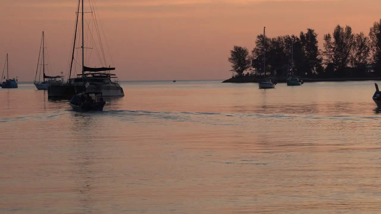 Beautiful landscape shot capturing shimmering sunset reflection on calm water surface with fishing boat cruising forward and luxurious yacht anchored in the bay langkawi island malaysia