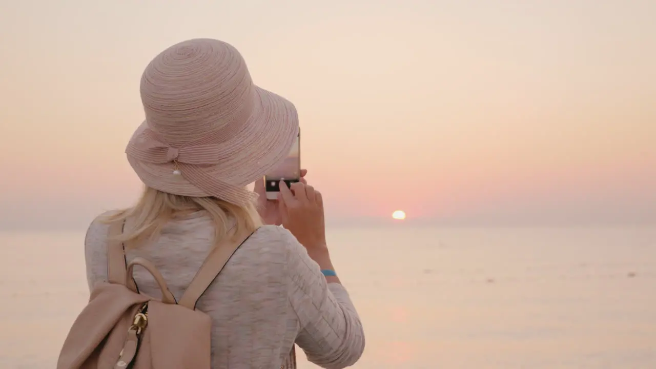 Young Woman Tourist In A Pink Hat Makes A Photo Of The Rising Sun On The Sea