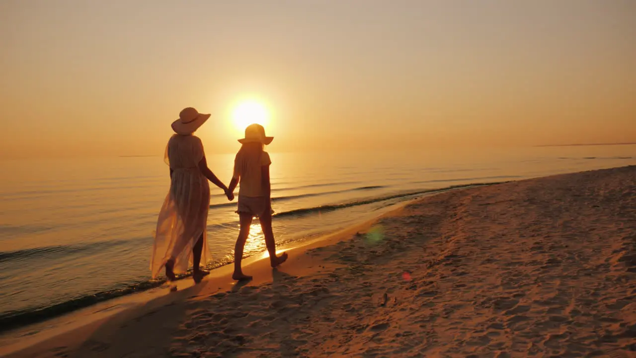 Mom And Daughter Are Walking By The Sea At Sunset Holiday With A Child Concept Steadicam Shot