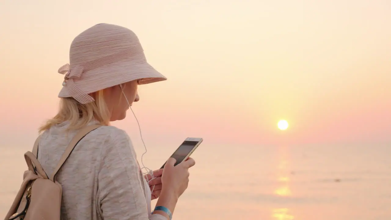 Not A Minute Without A Phone The Girl Is Standing On The Beach With A Pink Sky And Sky Looking At Th