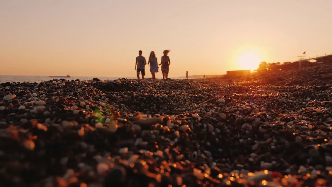 A Family With A Child Jogs Along The Surf Line To The Sea At Sunset