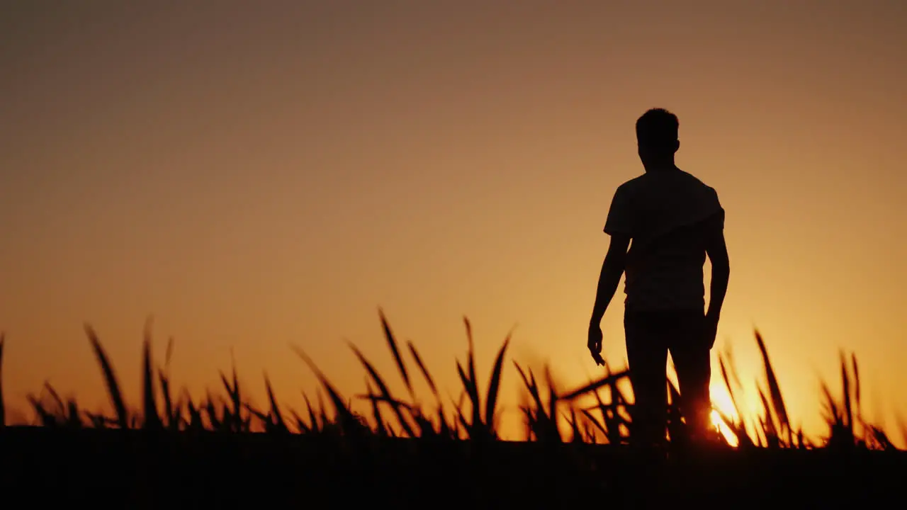 Silhouette A Young Man Enjoys The Fresh Air And Admires The Sunset He Holds His Hands Behind The Bac