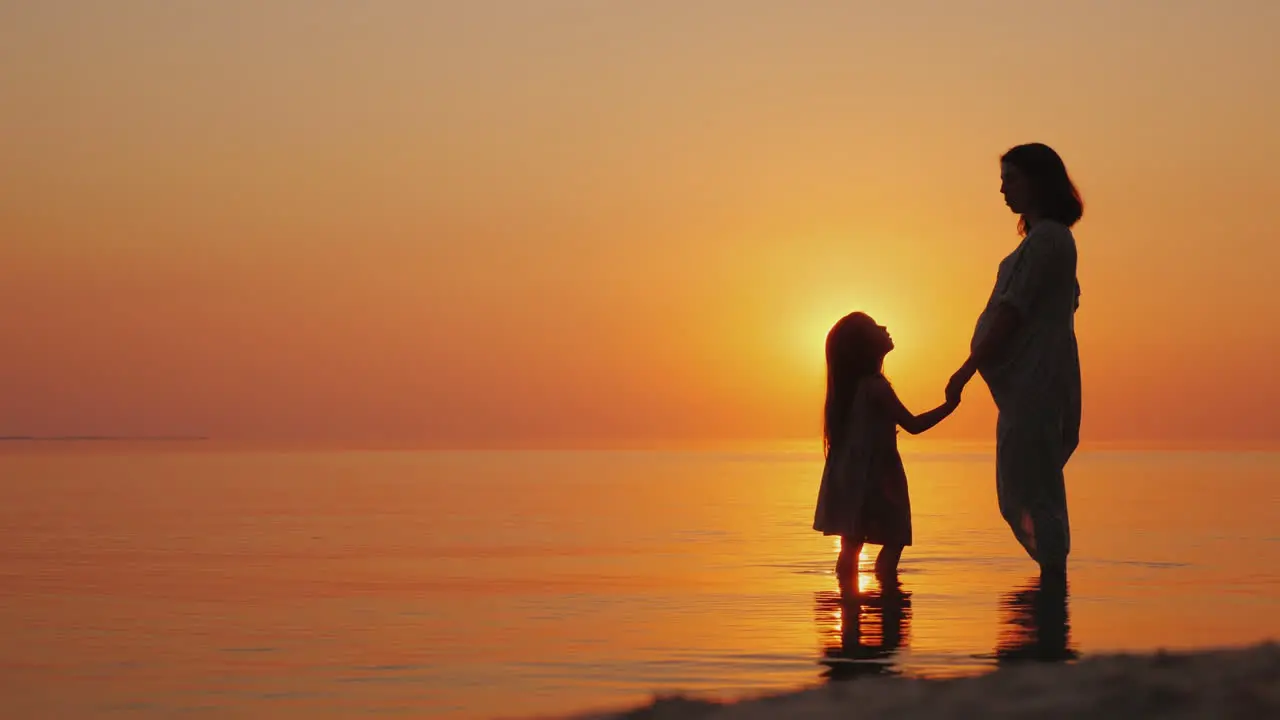 A Pregnant Woman Gently Kisses Her Eldest Daughter Beautiful Silhouettes Near The Sea At Sunset Wait