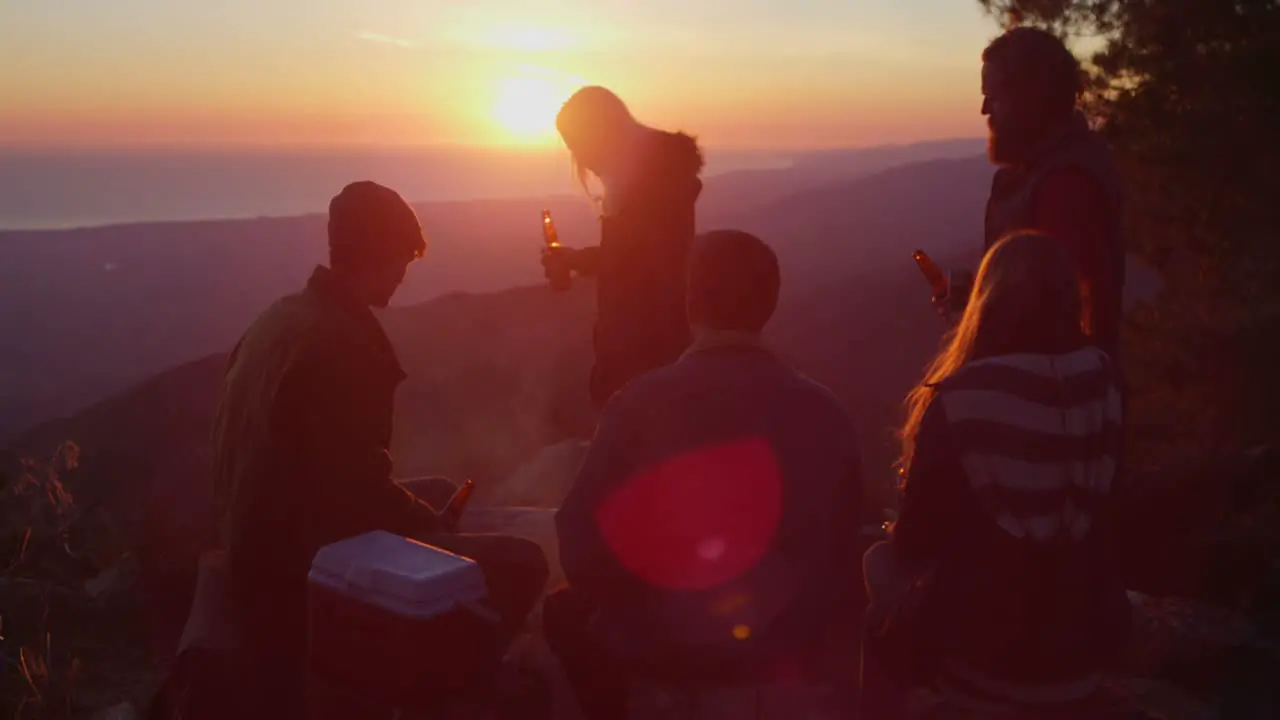 A group of friends drink beer at a campsite as the sun sets