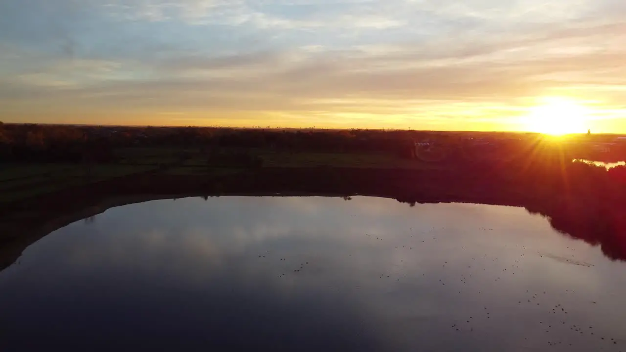 Cloudscape reflects on clear lake water during golden sunset aerial drone view