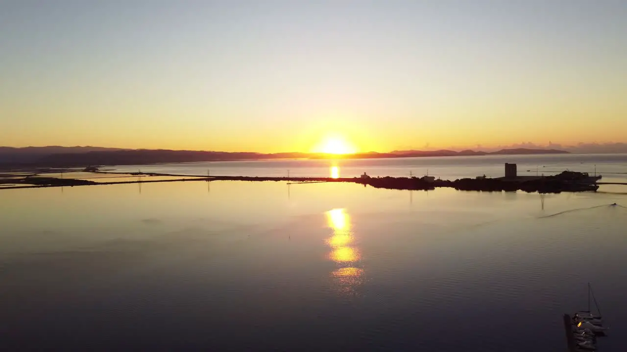 Stunning aerial of sunrise over peaceful calm lagoon water flying forward