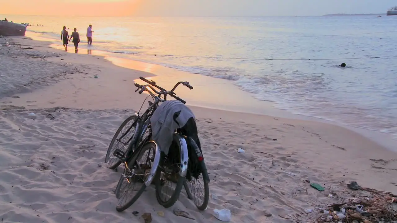 Sunset shot along a beach with two bicycles parked on the shore and children playing in distance