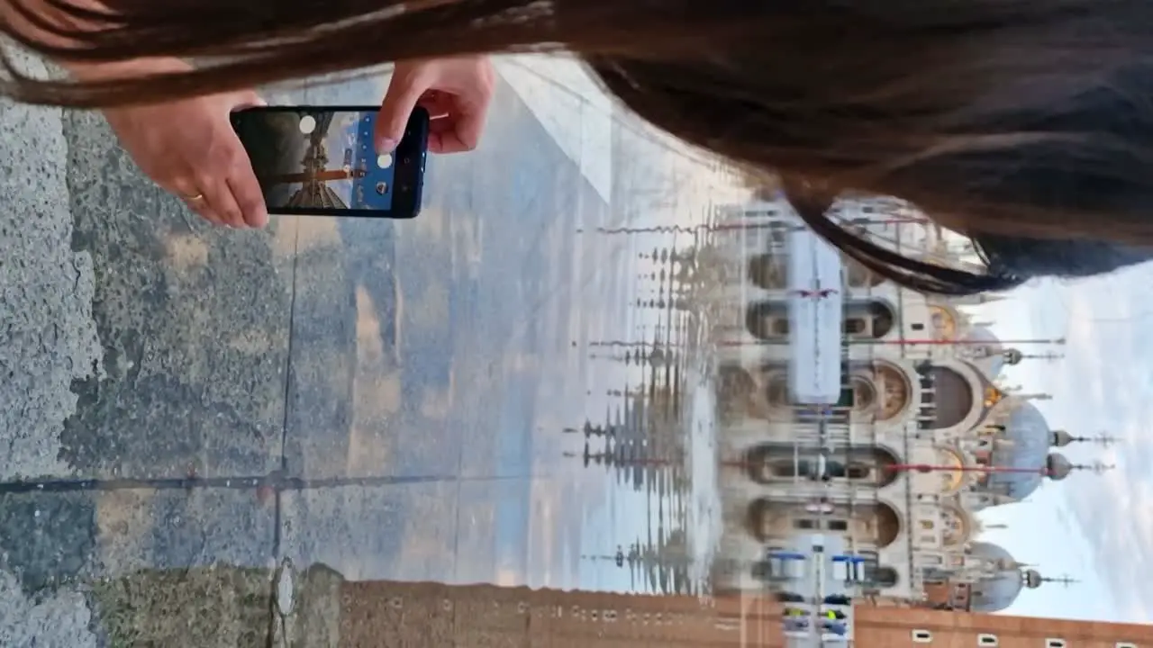 Young traveler woman taking reflection pictures of Basilica di San Marco during Acqua Alta period vertical