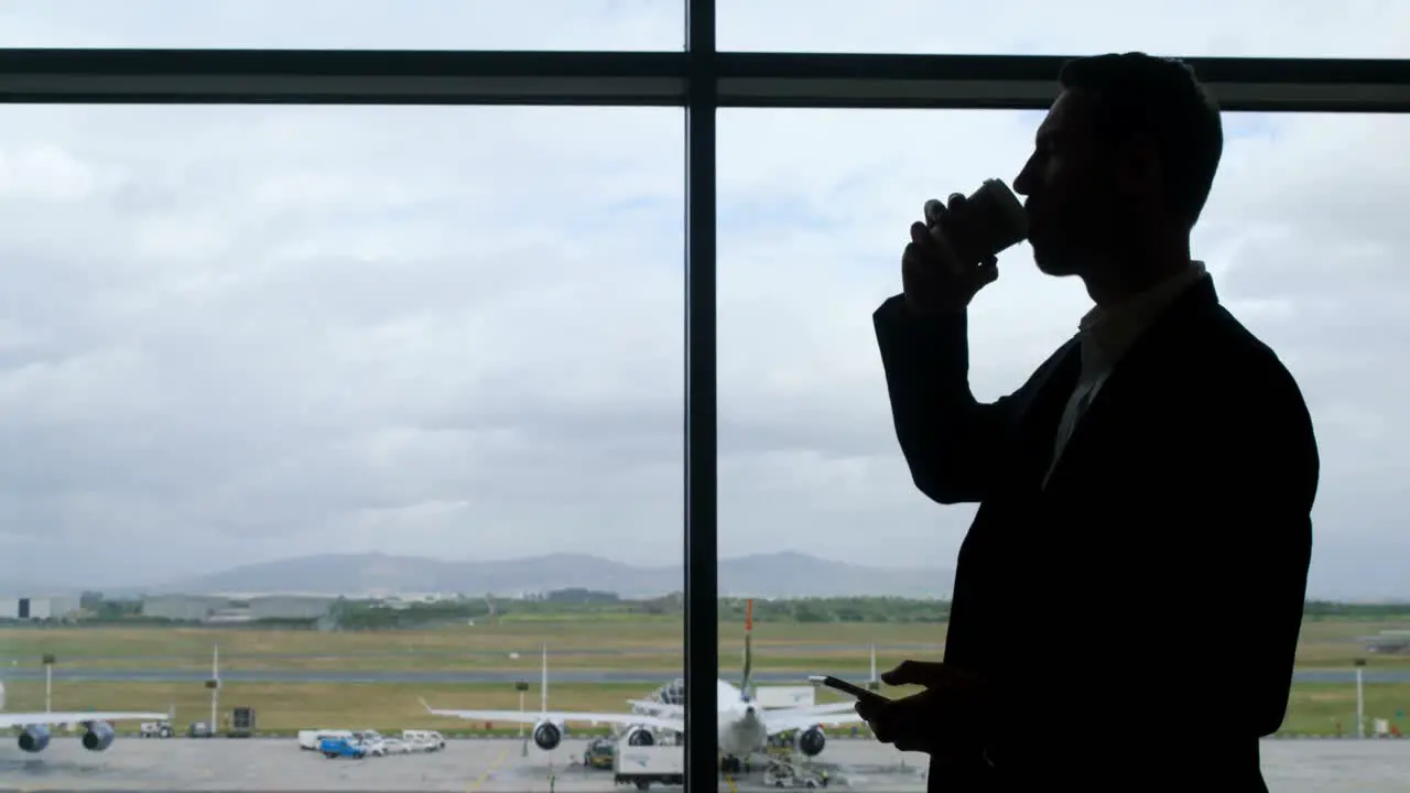 Businessman drinking coffee and holding mobile phone at airport 