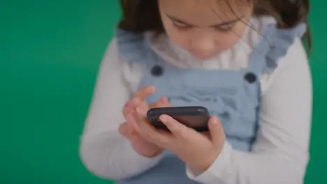 Studio Portrait Of Young Girl On ASD Spectrum Playing With Mobile Phone On Green Background 1