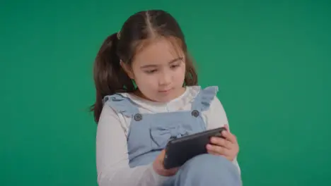 Studio Portrait Of Young Girl On ASD Spectrum Playing With Mobile Phone On Green Background 3