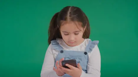 Studio Portrait Of Young Girl On ASD Spectrum Playing With Mobile Phone On Green Background