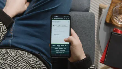 Overhead Shot Of Person At Home Shopping Online Looking At John Lewis Website On Mobile Phone