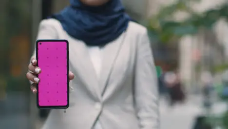 Close Up Of Muslim Businesswoman Holding Mobile Phone With Blank Screen To Camera Standing Outside Office In City