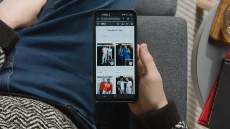 Overhead Shot Of Person At Home Shopping Online Looking At Asos Website On Mobile Phone 1