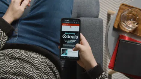 Overhead Shot Of Person At Home Shopping Online Looking At Target Website On Mobile Phone On Black Friday