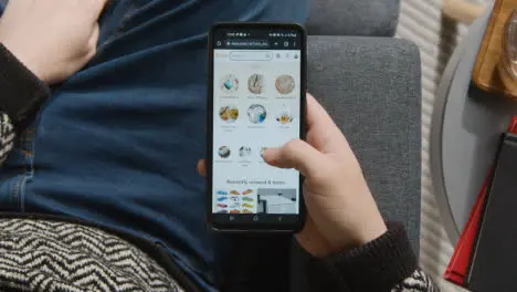 Overhead Shot Of Person At Home Shopping Online Looking At Etsy Website On Mobile Phone