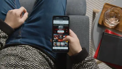 Overhead Shot Of Person At Home Shopping Online Looking At Shein Website On Mobile Phone On Black Friday