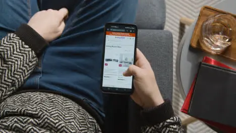 Overhead Shot Of Person At Home Shopping Online Looking At Wayfair Website On Mobile Phone On Black Friday