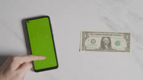 Overhead Currency Shot Of US 1 Dollar Bill Next To Person Using Green Screen Mobile Phone