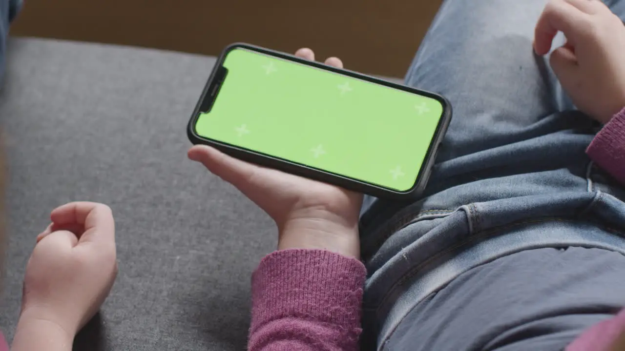 Close Up Of Two Children Sitting On Sofa At Home Looking At Green Screen Mobile Phone 3