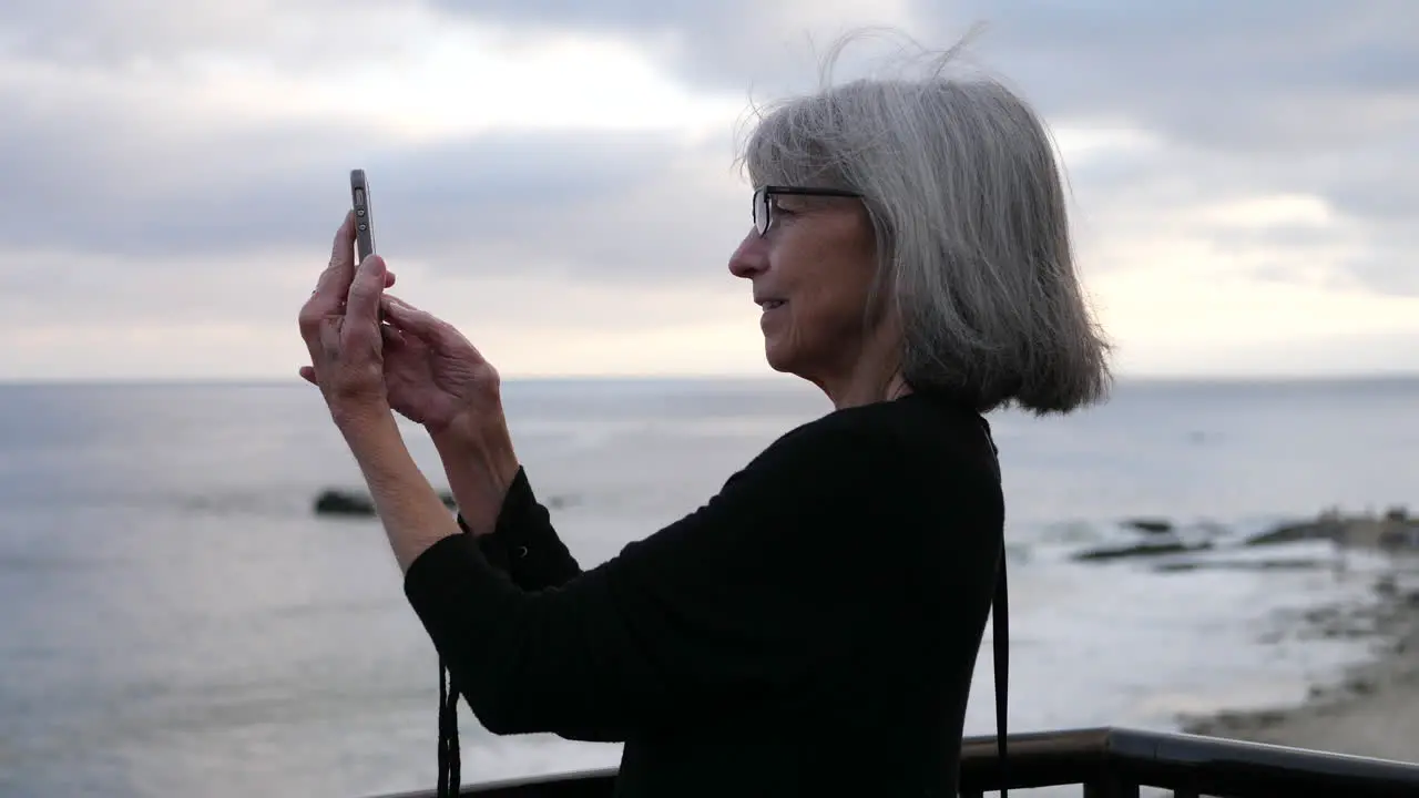 An old lady on vacation happy and smiling while taking a picture of the city and ocean in Laguna Beach California SLOW MOTION