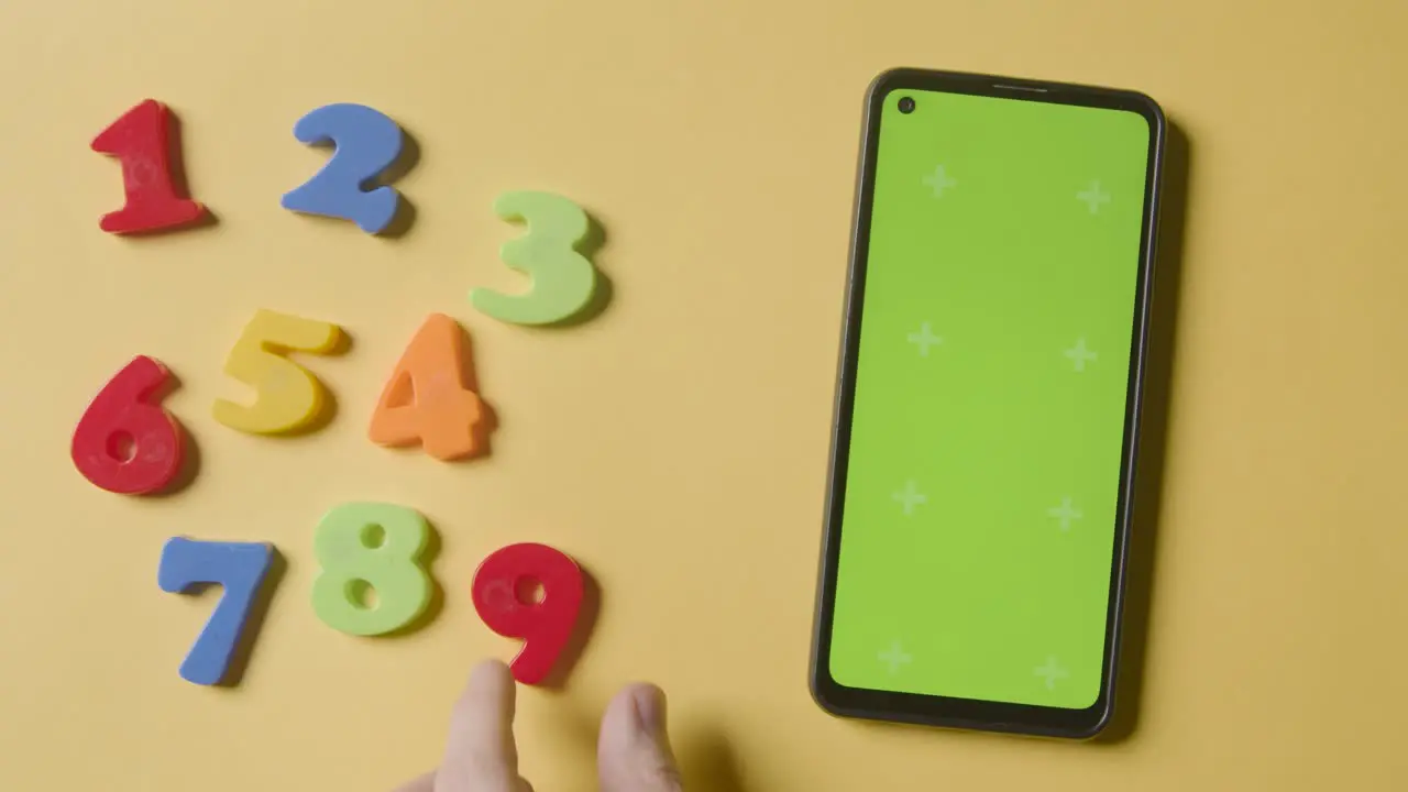 Studio Overhead Shot Of Plastic Numbers Arranged In Order With Green Screen Mobile Phone On Yellow Background 