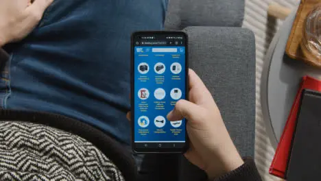 Overhead Shot Of Person At Home Shopping Online Looking At Bestbuy Website On Mobile Phone