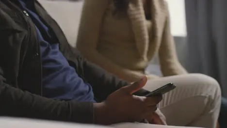 Close Up Of Couple At Home Sitting On Sofa In Lounge Having Argument Over What Man Is Looking At On Mobile Phone