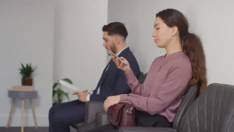 Male And Female Candidates In Office Waiting For Job Interview Looking At Mobile Phone And Reading Notes 5